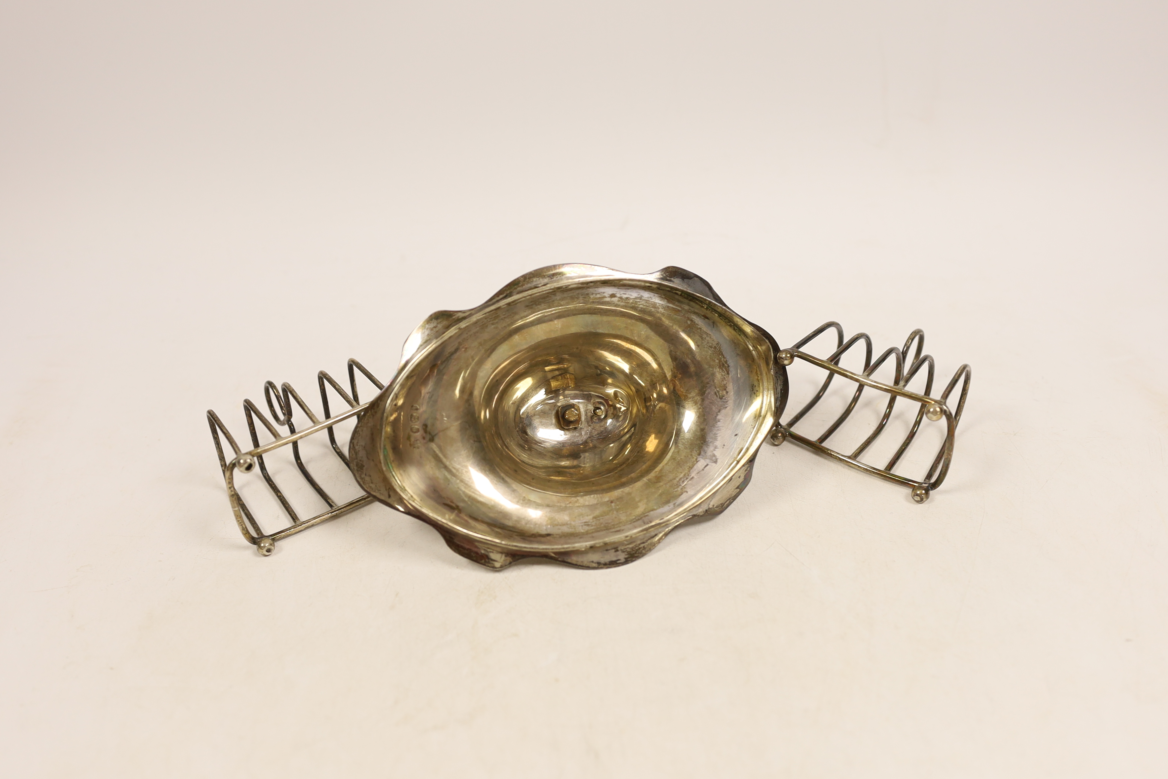 Two small silver four division wirework toast racks and a silver cover with handle, 6.6oz.